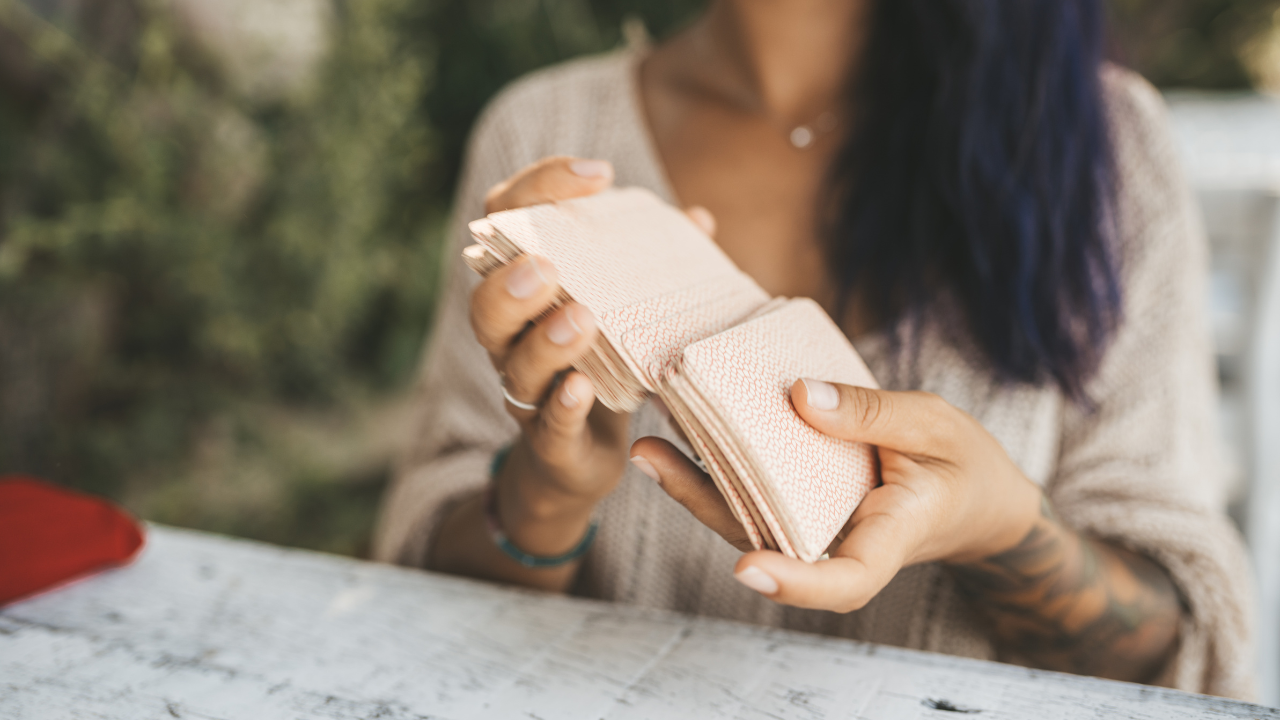 Tarot není předpověď budoucnosti. Jak skutečně pracuji s výklady žena míchá tarotové karty, jdou vidět jen její ruce, karty, trup a tmavé vlasy spadajkící pod ramena